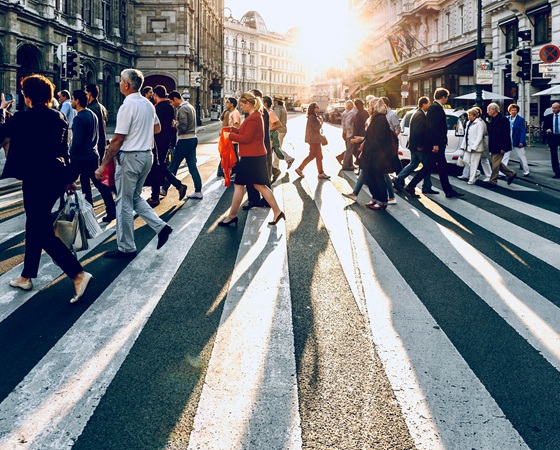 People crossing the street in a city with the sun setting in the background